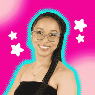 A portrait of Stary, smiling with her signature blue glasses, gold jewelry, and long box braids, dressed in a sleeveless black shirt.